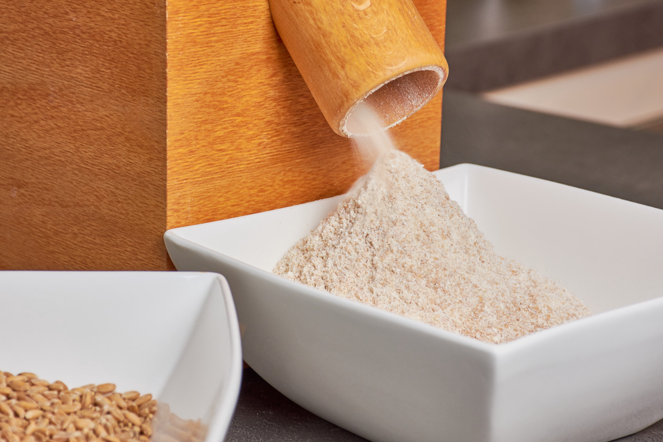White bowl being filled with a fresh-milled flour from a home mill.