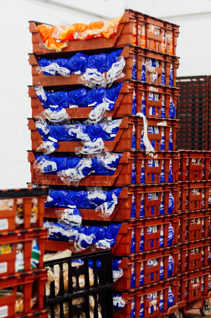 Stack of red crates containing blue and white plastic packages of bread in a warehouse setting